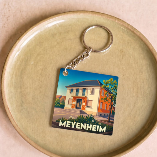 Porte-clés souvenir de la ville de Meyenheim avec une illustration stylisée d'un bâtiment local.