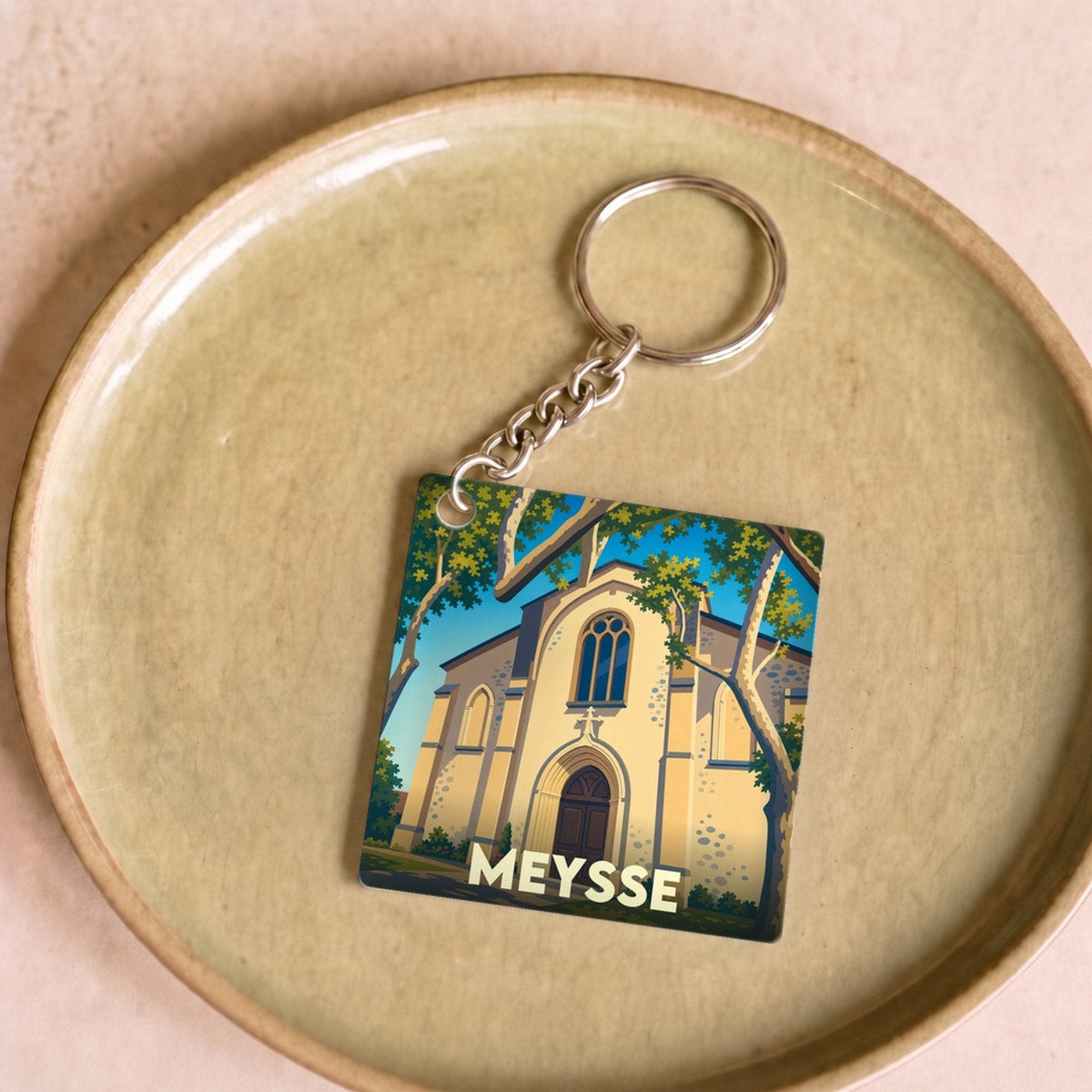 Porte-clés souvenir de la ville de Meysse avec une illustration stylisée de son église entourée d'arbres.