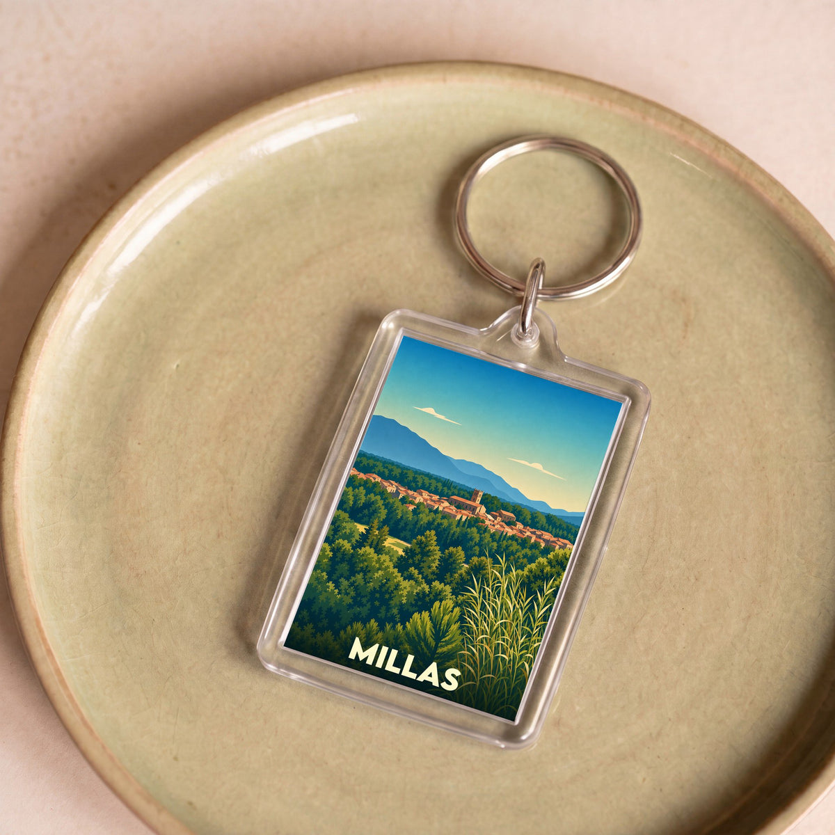 Porte-clés souvenir de la ville de Millas avec une illustration stylisée de son paysage.