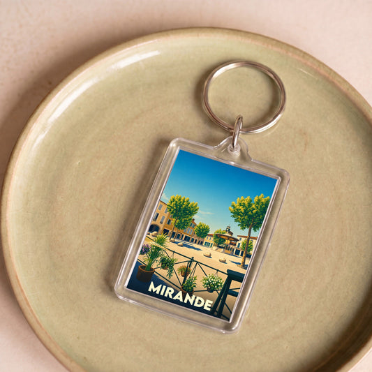 Porte-clés souvenir de la ville de Mirande avec une illustration stylisée de sa place principale.
