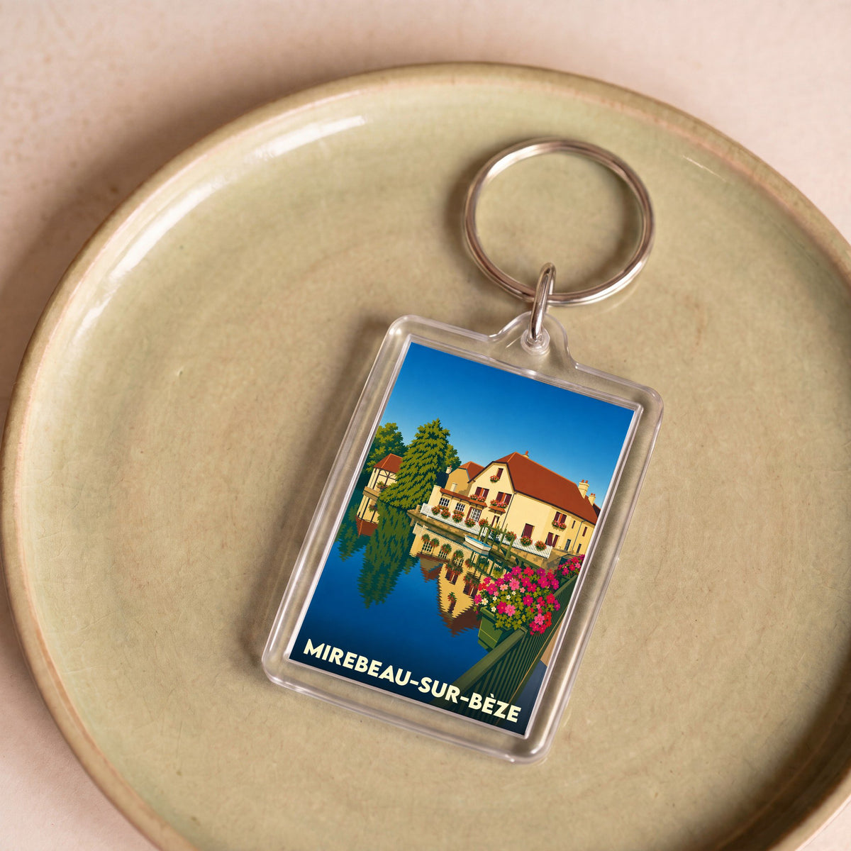 Porte-clés souvenir de la ville de Mirebeau-sur-Bèze avec une illustration stylisée d'une maison au bord de l'eau.