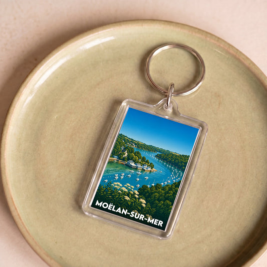 Porte-clés souvenir de la ville de Moëlan-sur-Mer avec une illustration stylisée d'un port côtier.
