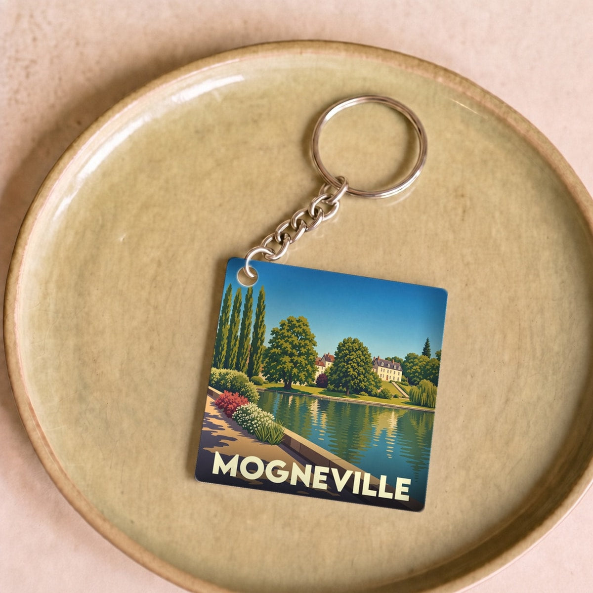Porte-clés souvenir de la ville de Mogneville avec une illustration stylisée d'un paysage de bord d'eau.