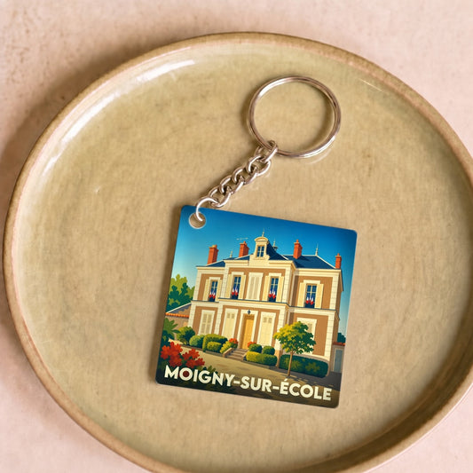 Porte-clés souvenir de la ville de Moigny-sur-École avec une illustration stylisée d'une grande demeure bourgeoise.