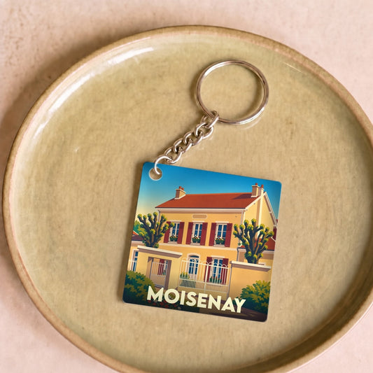 Porte-clés souvenir de la ville de Moisenay avec une illustration stylisée d'une maison traditionnelle.