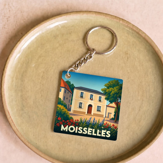Porte-clés souvenir de la ville de Moisselles avec une illustration colorée et stylisée d'une maison fleurie.