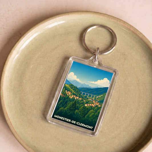 Porte-clés souvenir de la ville de Monestier-de-Clermont avec une illustration stylisée d'un paysage montagneux.