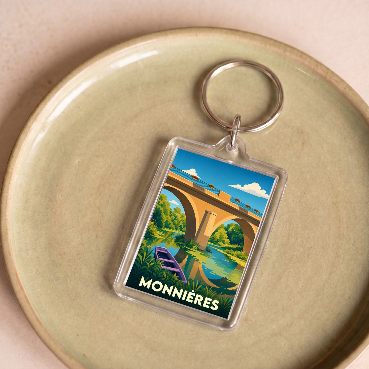 Porte-clés souvenir de la ville de Monnières avec une illustration stylisée d'un pont et d'une barque.