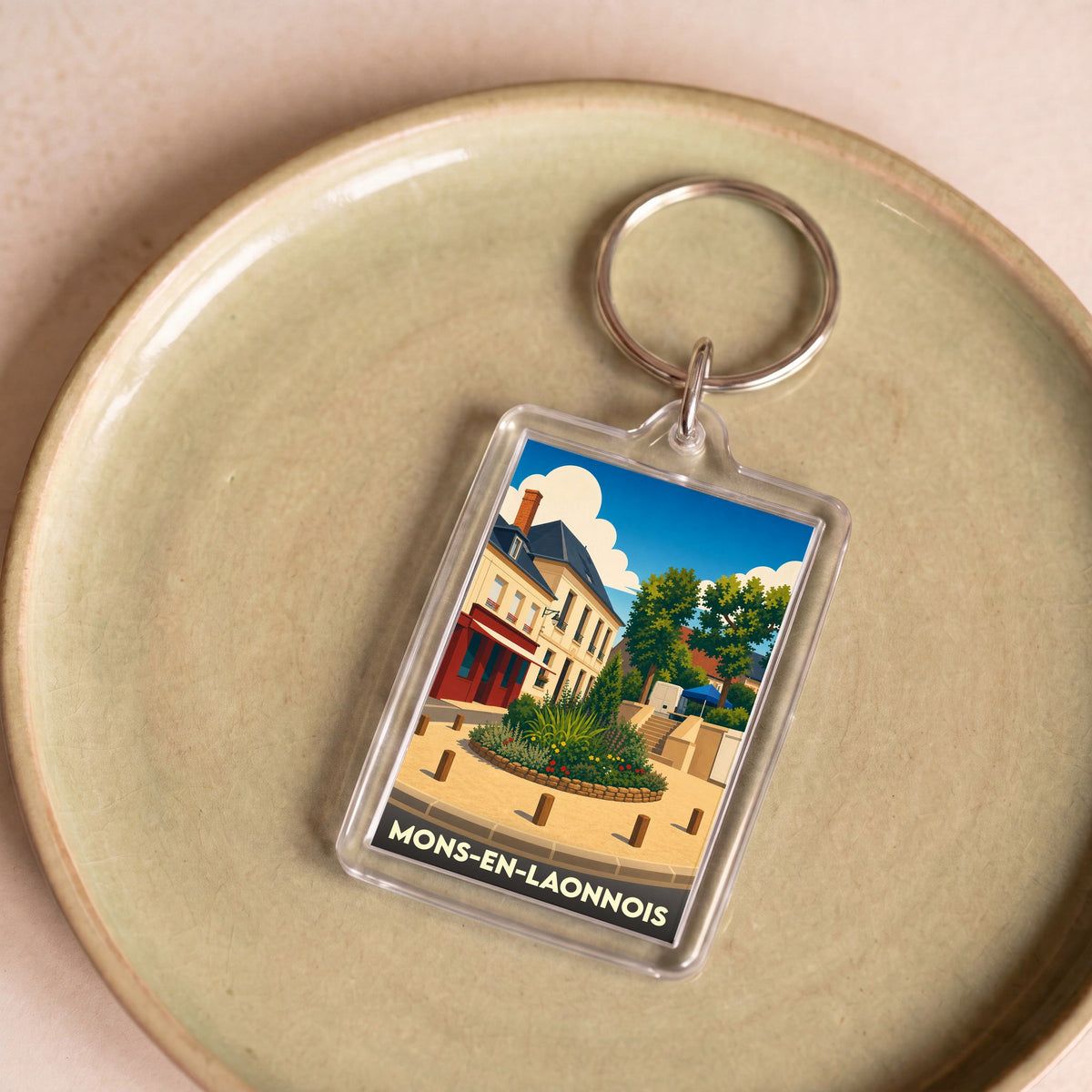 Porte-clés souvenir de la ville de Mons-en-Laonnois avec une illustration stylisée.