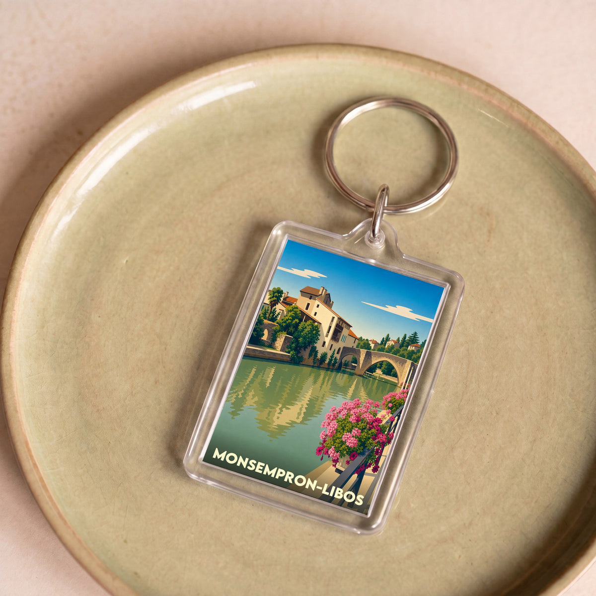 Porte-clés souvenir de la ville de Monsempron-Libos avec une illustration stylisée d'un paysage fluvial.