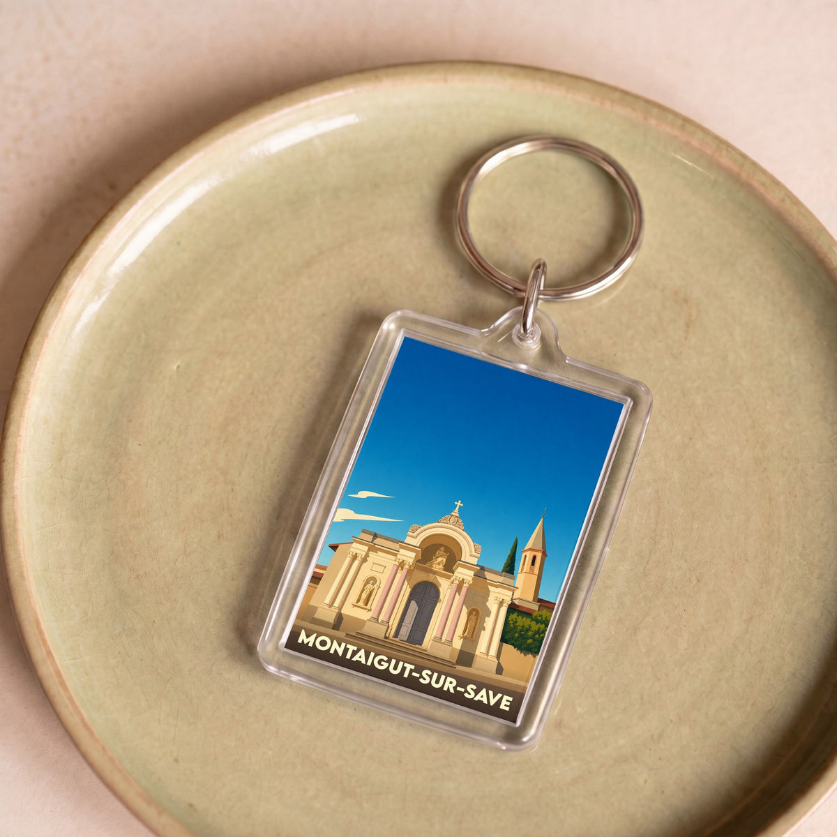 Porte-clés souvenir de la ville de Montaigut-sur-Save avec une illustration stylisée.