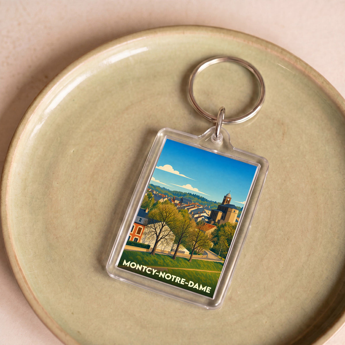 Porte-clés souvenir de la ville de Montcy-Notre-Dame avec une illustration stylisée.
