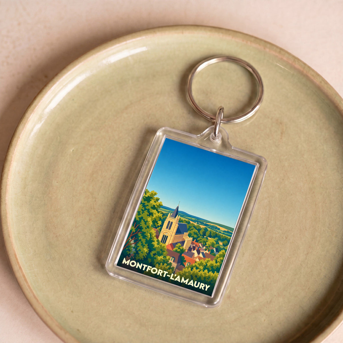 Porte-clés souvenir de la ville de Montfort-l'Amaury avec une illustration stylisée de son église entourée de verdure.