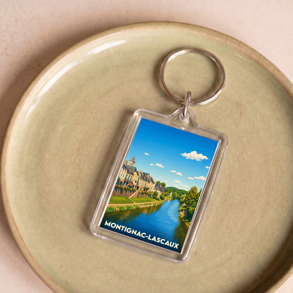 Porte-clés souvenir de Montignac-Lascaux avec une illustration stylisée de la ville et de sa rivière.