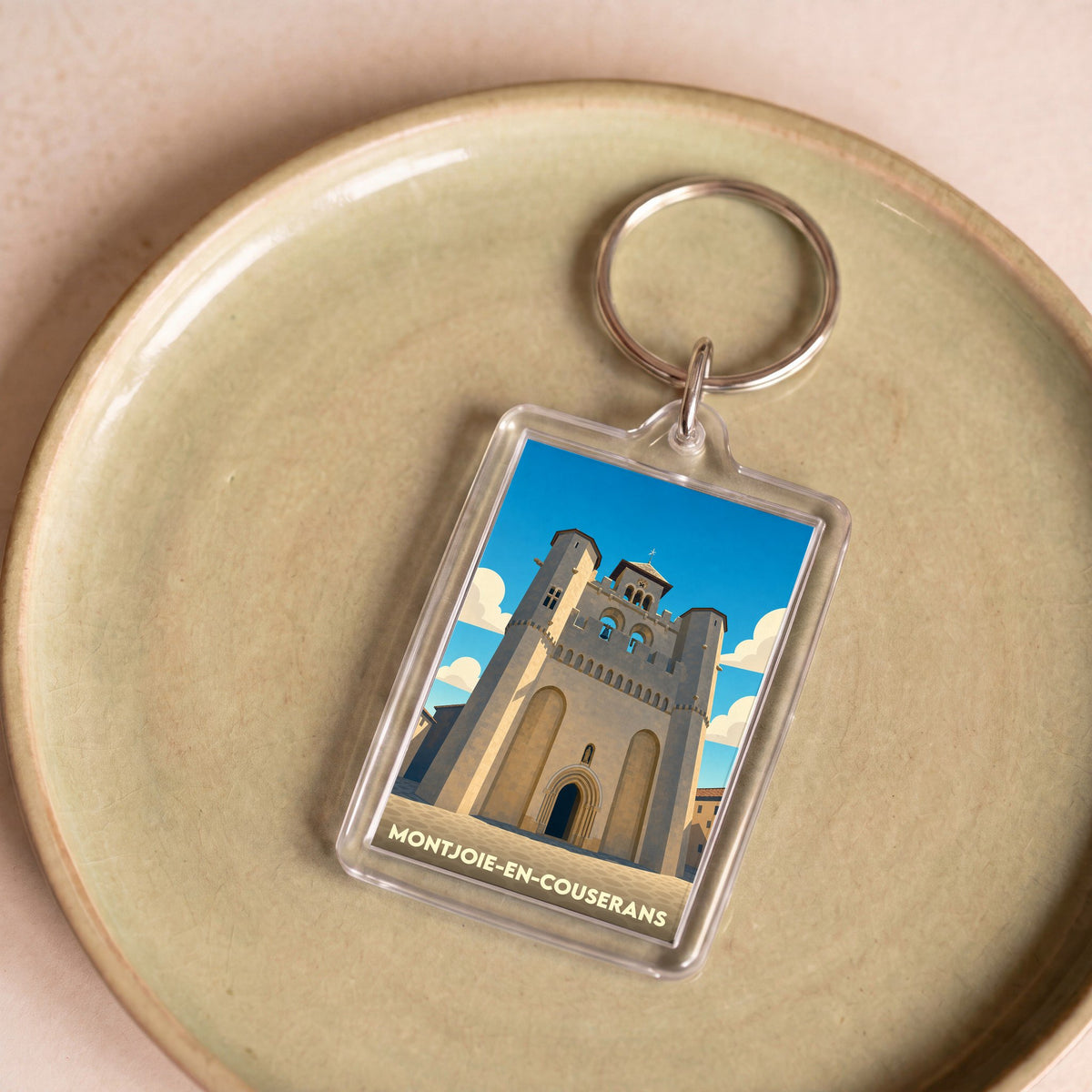 Porte-clés souvenir de la ville de Montjoie-en-Couserans avec une illustration stylisée de son église fortifiée.