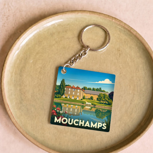 Porte-clés souvenir de la ville de Mouchamps avec une illustration stylisée d'un manoir se reflétant dans l'eau.