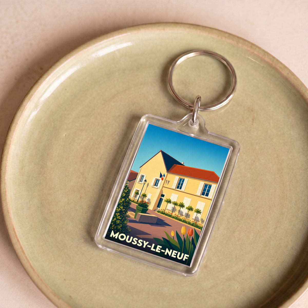 Porte-clés souvenir de la ville de Moussy-le-Neuf avec une illustration stylisée d'un bâtiment ensoleillé.
