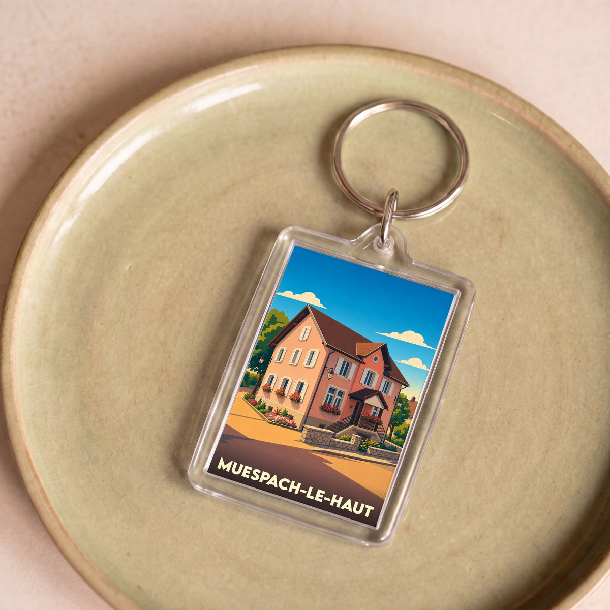Porte-clés souvenir de la ville de Muespach-le-Haut avec une illustration stylisée d'une maison alsacienne.
