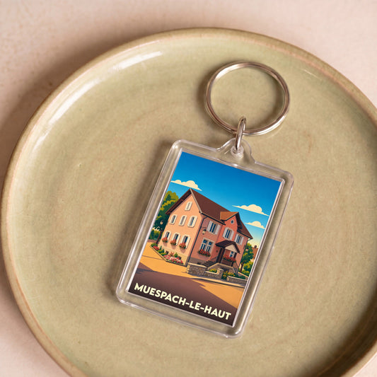 Porte-clés souvenir de la ville de Muespach-le-Haut avec une illustration stylisée d'une maison alsacienne.