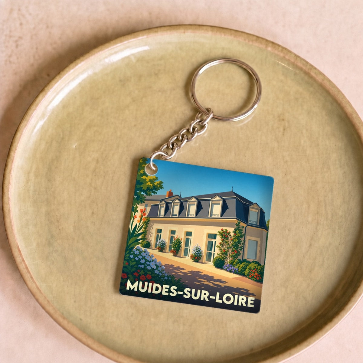 Porte-clés souvenir de la ville de Muides-sur-Loire avec une illustration stylisée d'une demeure fleurie.