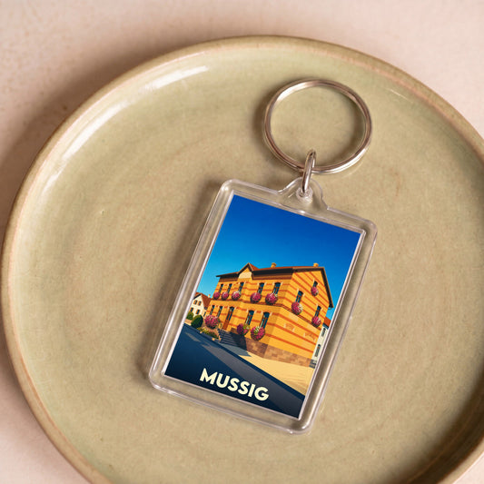 Porte-clés souvenir de la ville de Mussig avec une illustration stylisée de sa mairie fleurie.