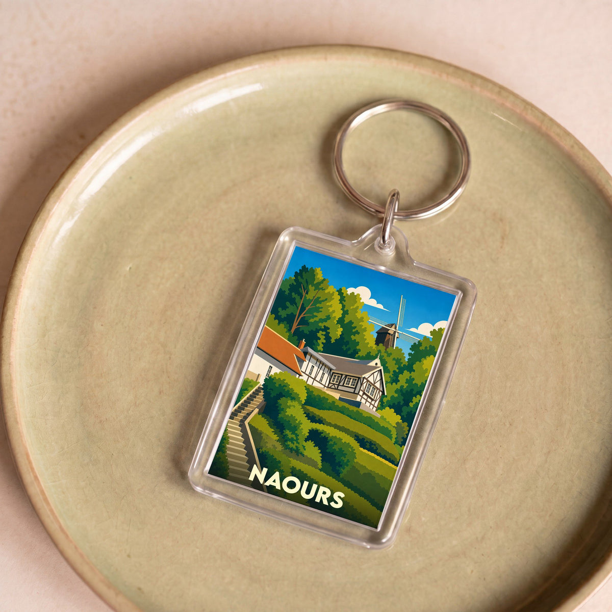Porte-clés souvenir de la ville de Naours avec une illustration stylisée d'un paysage verdoyant et d'un moulin.