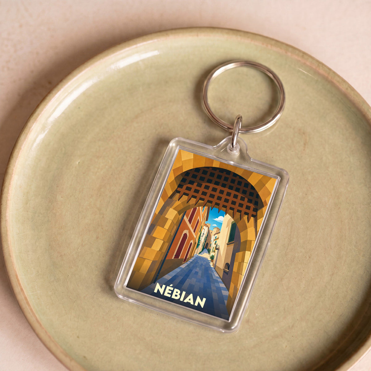 Porte-clés souvenir de la ville de Nébian avec une illustration stylisée d'une ruelle médiévale.