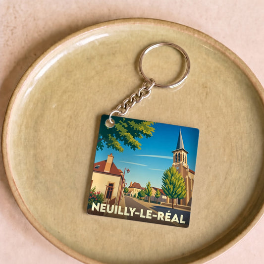 Porte-clés souvenir de la ville de Neuilly-le-Réal avec une illustration stylisée d'une rue du village et de son église.