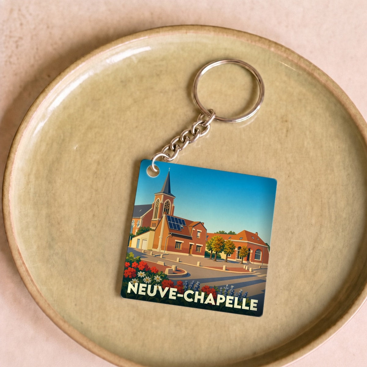 Porte-clés souvenir de la ville de Neuve-Chapelle avec une illustration stylisée de son église et de fleurs colorées.