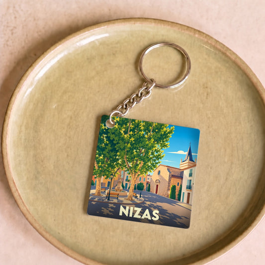 Porte-clés souvenir de la ville de Nizas avec une illustration stylisée de sa place ensoleillée.
