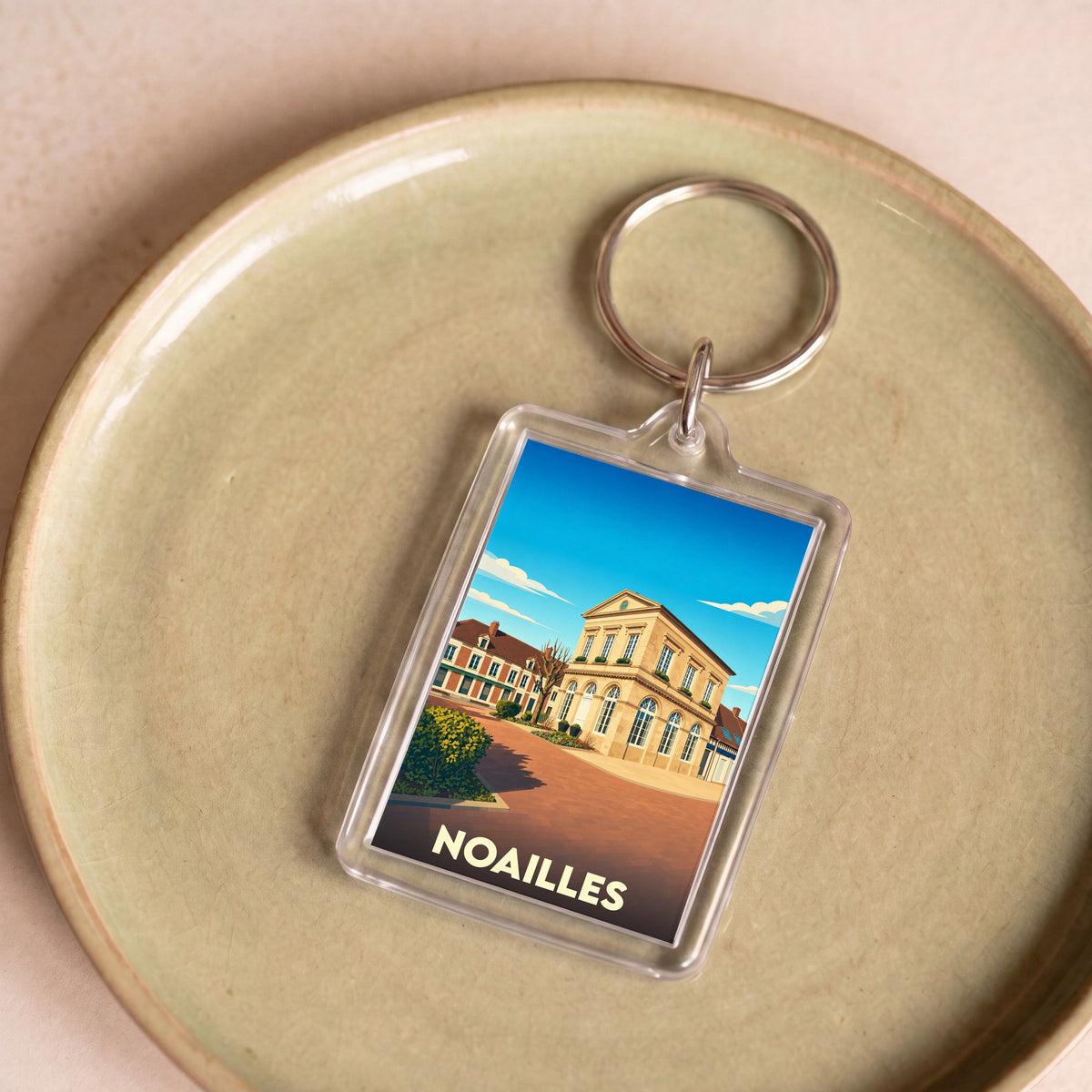 Porte-clés souvenir de la ville de Noailles avec une illustration stylisée.
