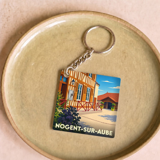Porte-clés souvenir de la ville de Nogent-sur-Aube avec une illustration stylisée de maisons à colombages.