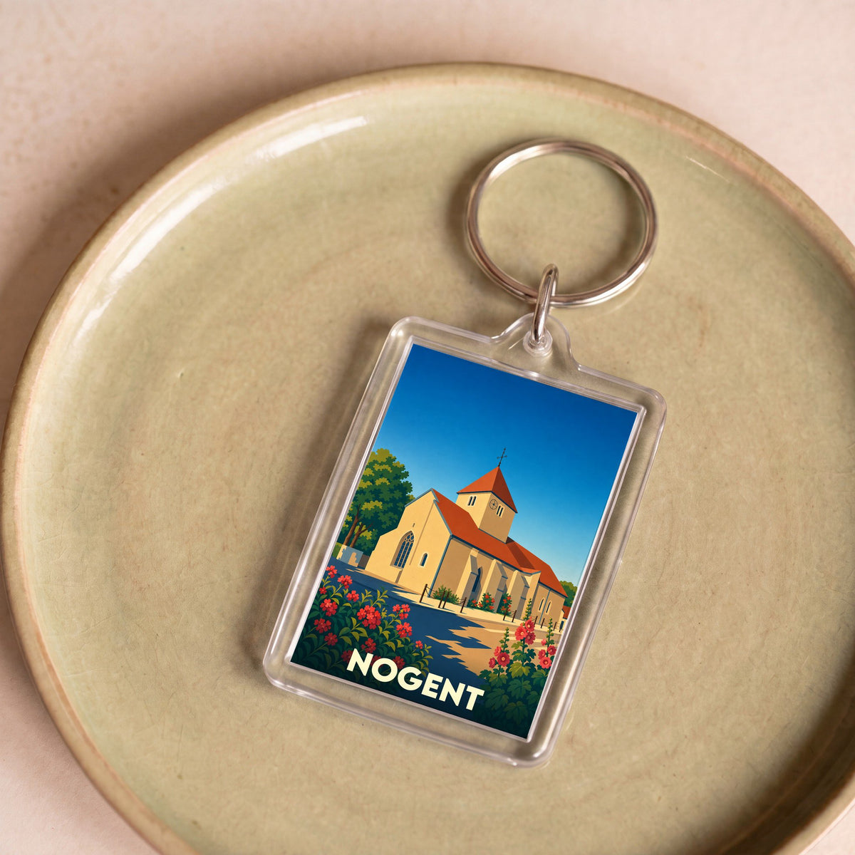 Porte-clés souvenir de la ville de Nogent avec une illustration stylisée de son église et de fleurs colorées.