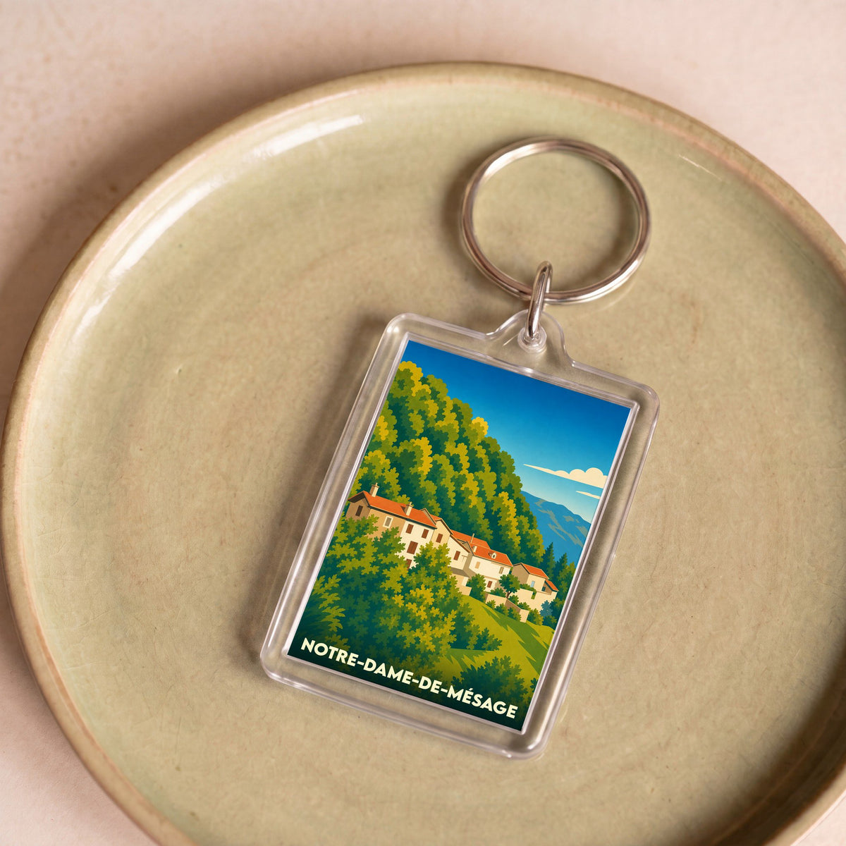Porte-clés souvenir de Notre-Dame-de-Mésage avec une illustration stylisée du village et de sa montagne boisée.