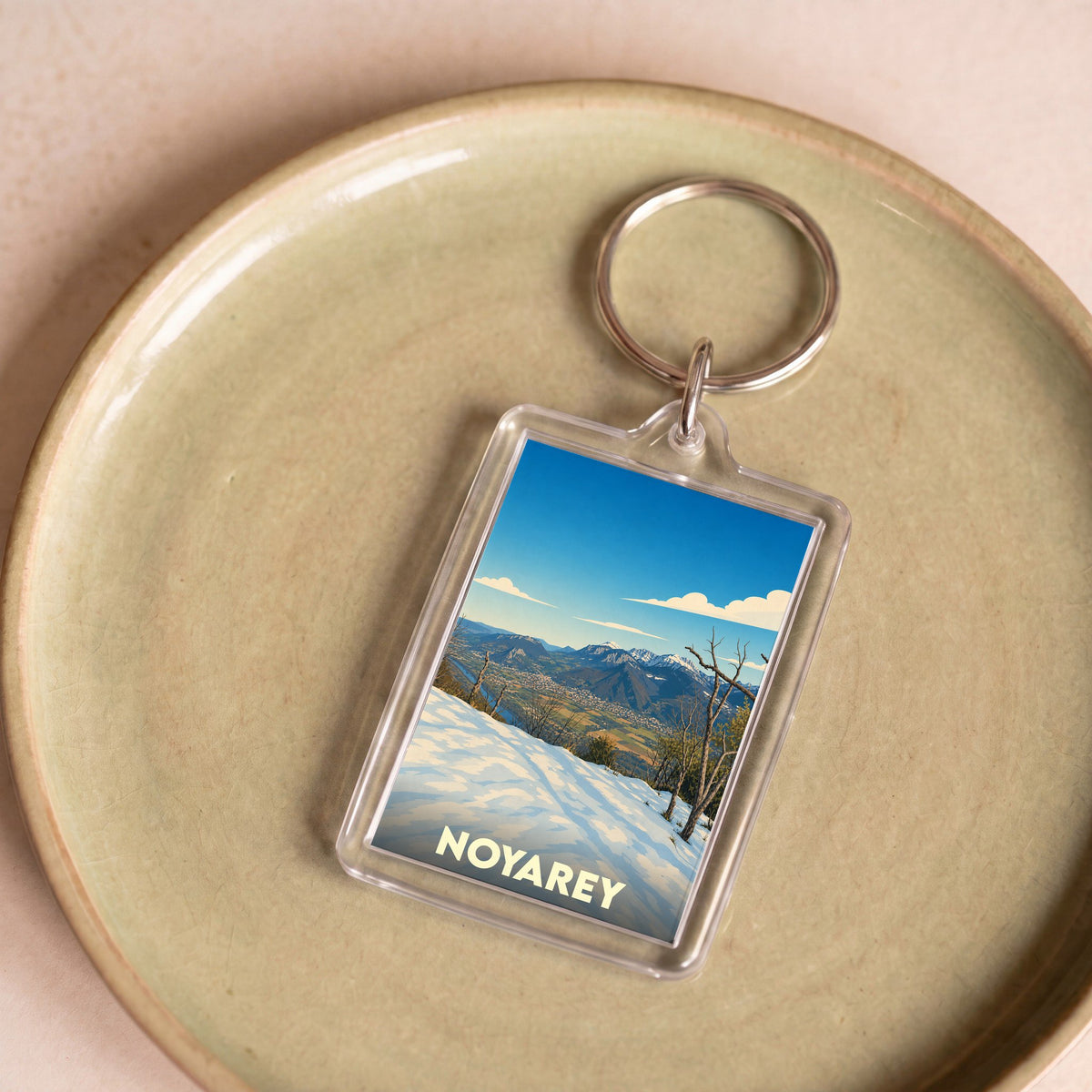 Porte-clés souvenir de la ville de Noyarey avec une illustration stylisée d'un paysage montagneux enneigé.