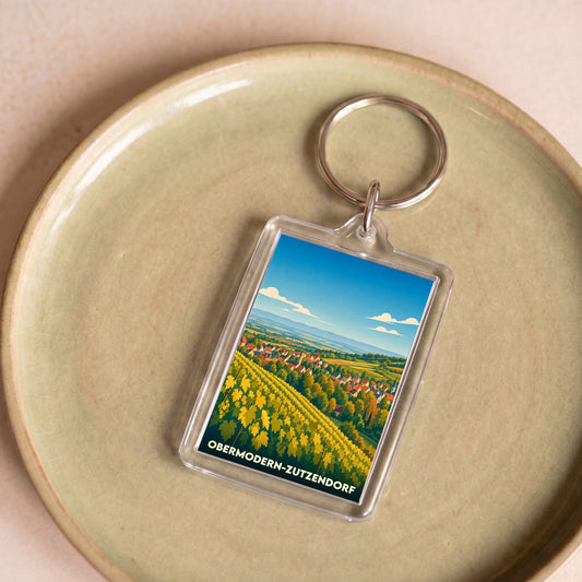 Porte-clés souvenir de la ville d'Obermodern-Zutzendorf illustré d'un paysage de vignobles et de village.