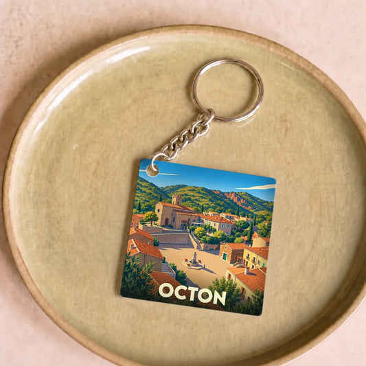 Porte-clés souvenir de la ville d'Octon illustrant un village méditerranéen ensoleillé.
