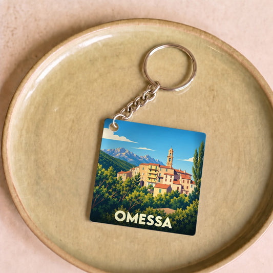 Porte-clés souvenir de la ville d'Omessa avec une illustration stylisée d'un village corse en montagne.