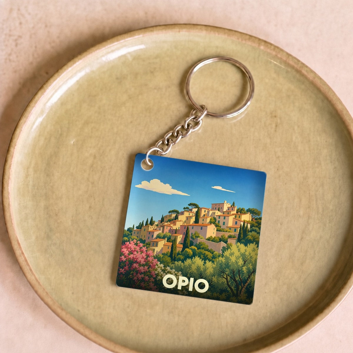 Porte-clés souvenir de la ville d'Opio avec une illustration stylisée d'un village provençal niché dans la végétation.
