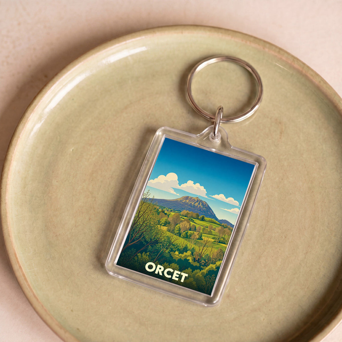 Porte-clés souvenir de la ville d'Orcet avec une illustration stylisée d'un paysage de montagne.