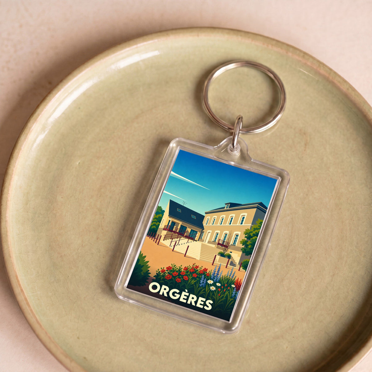 Porte-clés souvenir de la ville d'Orgères avec une illustration stylisée de bâtiments locaux et de fleurs.