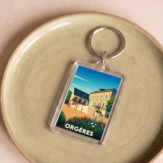 Porte-clés souvenir de la ville d'Orgères avec une illustration stylisée de bâtiments locaux et de fleurs.