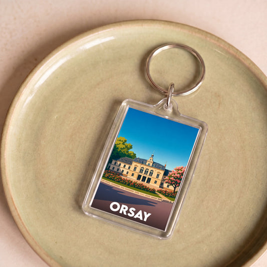 Porte-clés souvenir de la ville de Orsay avec une illustration stylisée du Musée d'Orsay au bord de la Seine.