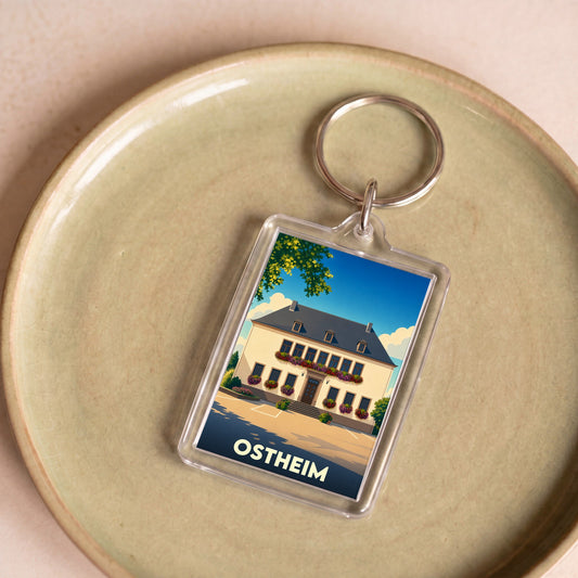 Porte-clés souvenir de la ville d'Ostheim avec une illustration stylisée d'un bâtiment fleuri.