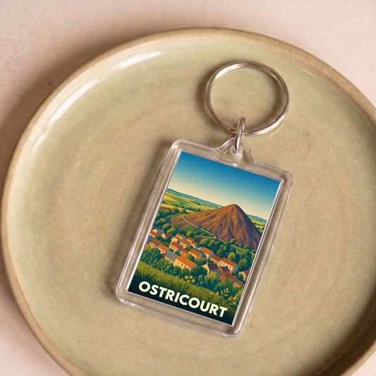 Porte-clés souvenir de la ville d'Ostricourt avec une illustration stylisée d'un terril dominant le village.