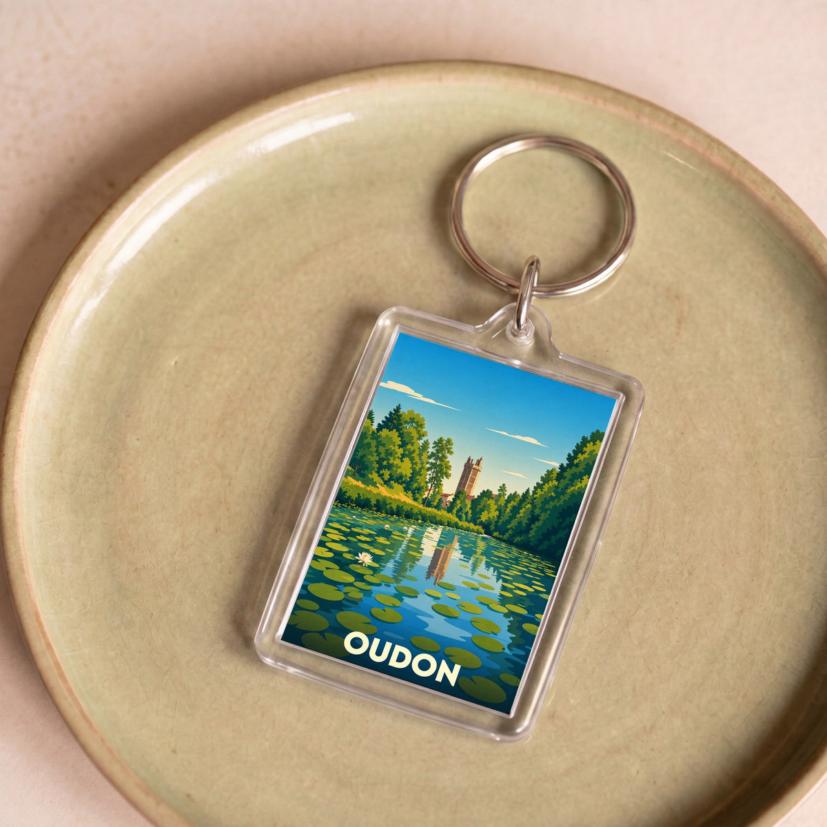 Porte-clés souvenir de la ville de Oudon avec une illustration stylisée d'un étang et son château.