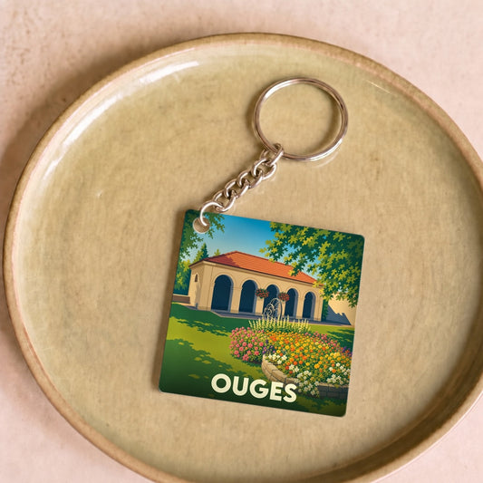 Porte-clés souvenir de la ville de Ouges avec une illustration stylisée d'un bâtiment à arcades et de jardins fleuris.