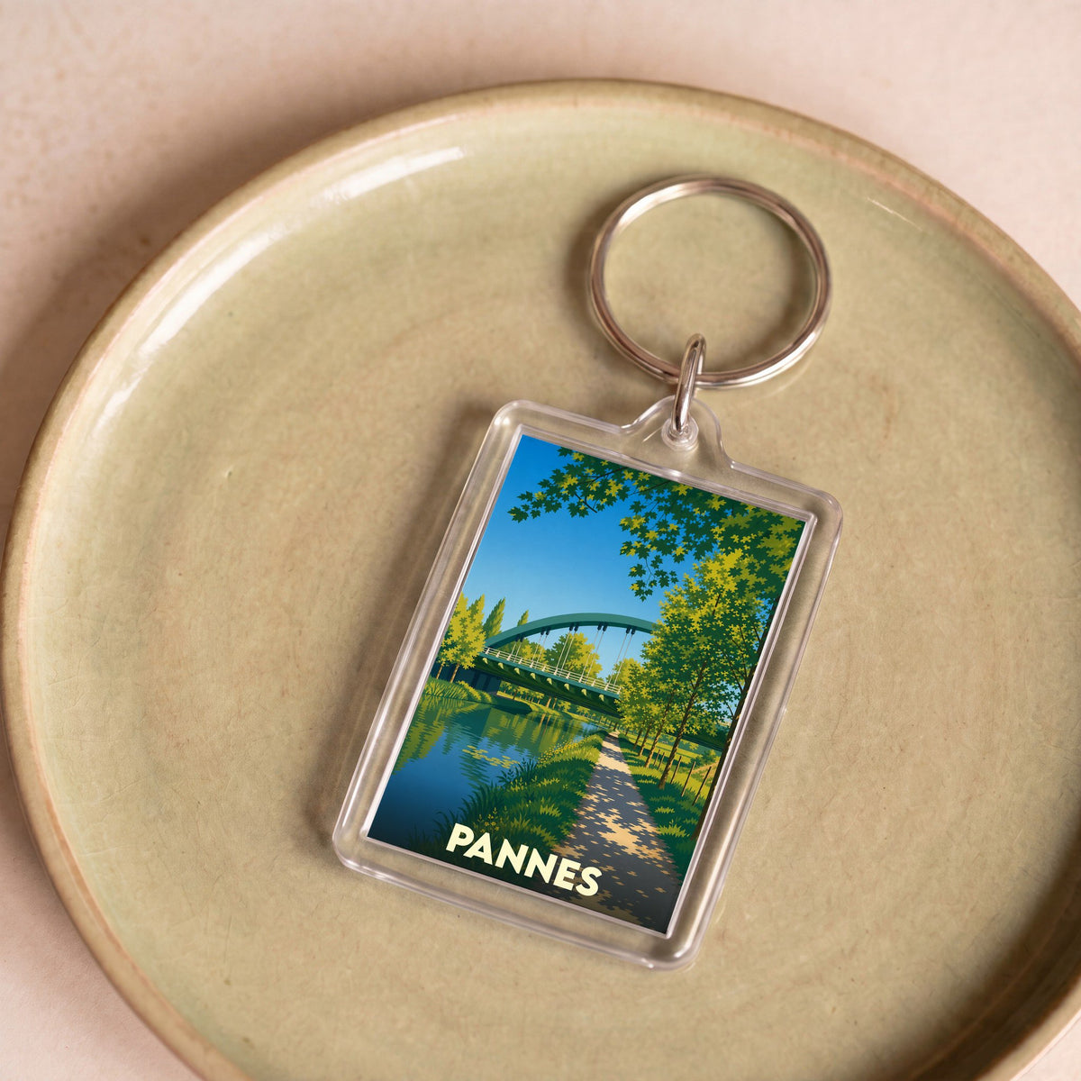 Porte-clés souvenir de la ville de Pannes avec une illustration stylisée d'un pont au-dessus de l'eau.
