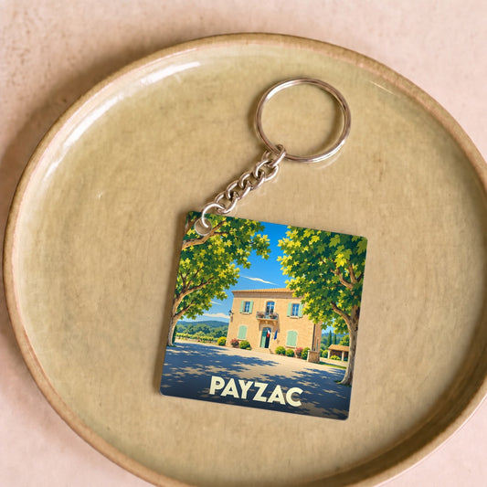 Porte-clés souvenir de la ville de Payzac avec une illustration stylisée d'une bâtisse ensoleillée.