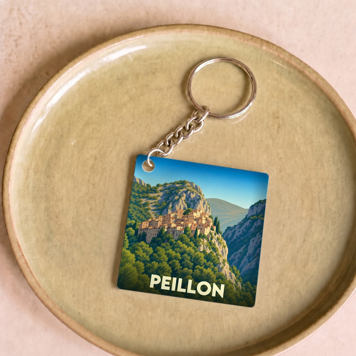 Porte-clés souvenir de la ville de Peillon avec une illustration stylisée d'un village perché.